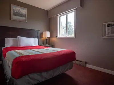 a bedroom with a bed with a red blanket and a window at Best Budget Inn & Suites Kamloops in Kamloops