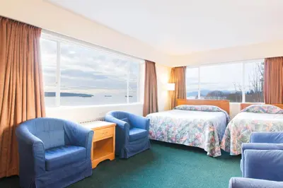 a hotel room with two beds and chairs and a window at English Bay Hotel in Vancouver
