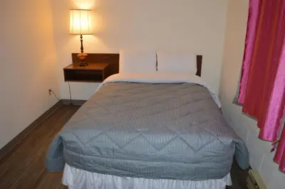 a bed in a small room with a lamp on a table at A1 Motel And Campground in Bassano