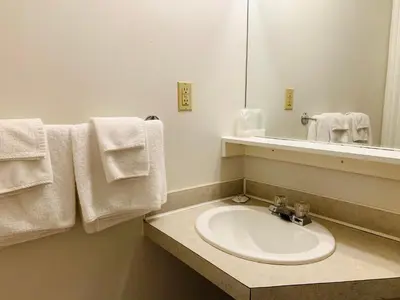 a bathroom with a sink and a mirror and towels at Traveler's Motel Penticton in Penticton
