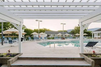 a pool at a resort with tables and chairs at Balcomo, a Ramada by Wyndham in Penticton