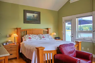 a bedroom with a bed and a chair and a window at Birds of a Feather Victoria Oceanfront Studio Suites in Colwood