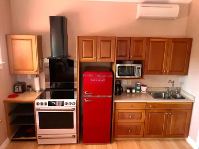 a red refrigerator in a small kitchen with wooden cabinets at Birds of a Feather Victoria Oceanfront Studio Suites in Colwood