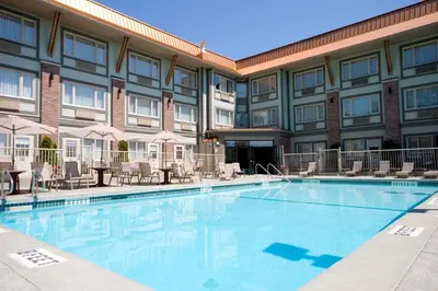 a pool in front of a hotel with chairs and tables at Holiday Inn Victoria - Elk Lake by IHG in Victoria