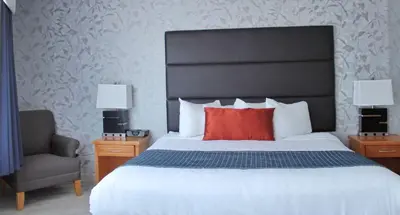 a bedroom with a bed with a red pillow and a chair at Best Western Plus Regency Inn and Conference Centre in Abbotsford