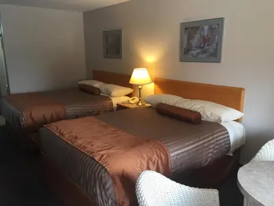 two beds in a hotel room with a lamp and a chair at Avalon Inn in Osoyoos