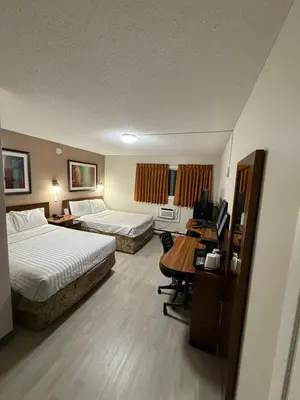a hotel room with two beds and a desk at Canadas Best Value Inn Kelowna in Kelowna