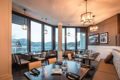 a restaurant with tables and chairs and large windows at Prestige Mountain Resort Rossland in Rossland