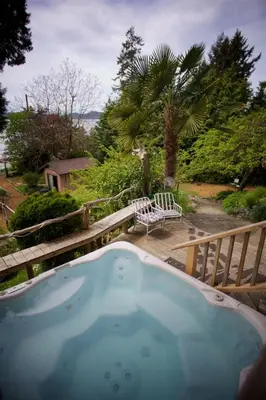a jacuzzi tub on a deck with a bench at Halfmoon Haven Beach Cottage or Oceanview Suite in Halfmoon Bay