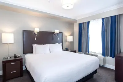 a bedroom with a large white bed with blue curtains at Sandman Signature Langley Hotel in Langley