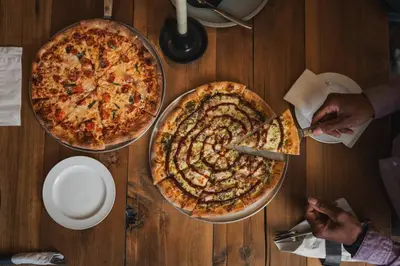 two pizzas on a wooden table with someone cutting a pizza at Predator Ridge Resort in Vernon