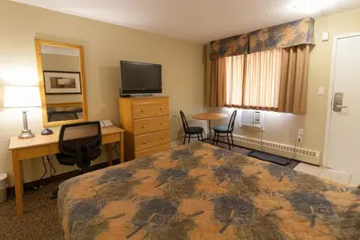 a hotel room with a bed and a desk and a tv at BCMInns - Fort McMurray - Rusty's in Fort McMurray
