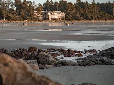 a beach with rocks and a house in the background at Long Beach Lodge Resort in Tofino