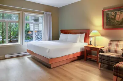 a bedroom with a bed and a chair and a window at Long Beach Lodge Resort in Tofino