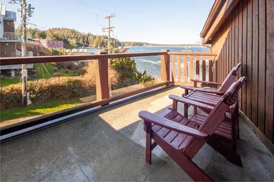 a wooden bench sitting on a balcony looking out at the water at Himwitsa Lodge in Tofino