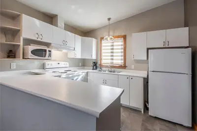 a kitchen with white cabinets and a white refrigerator at Himwitsa Lodge in Tofino