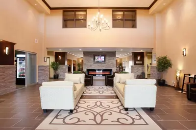 a lobby with two white chairs and a fireplace at Vegreville Suites in Vegreville