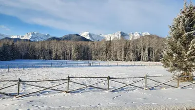 a fence in a snow covered field with mountains at Black Cat Guest Ranch in Brule Mines