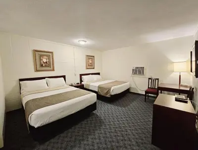 a hotel room with two beds and a desk at Canadian Motor Inn in Grande Prairie