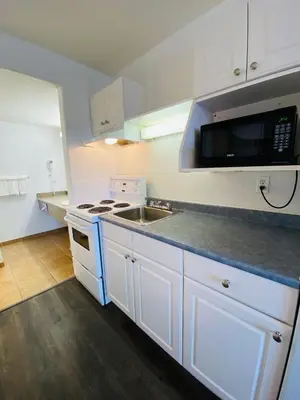 a kitchen with white cabinets and a sink and a microwave at Super 8 by Wyndham 100 Mile House in One Hundred Mile House