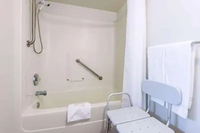 a white bathroom with a tub and a chair in it at Super 8 by Wyndham 100 Mile House in One Hundred Mile House