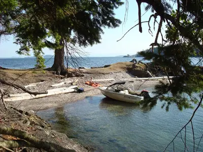 a boat sitting on the shore of a body of water at Sticks and Stones Cottage-Arbutus Grove in Galiano