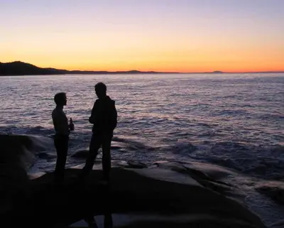 two people standing on the beach watching the sunset at Sticks and Stones Cottage-Arbutus Grove in Galiano