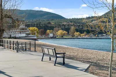 a bench sitting on a sidewalk next to a river at Okanagan Lakefront Resort in Penticton