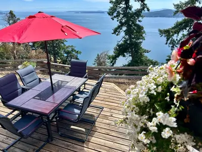 a wooden deck with a table with a red umbrella at Shangri-La Oceanfront vacation home in Pender Island