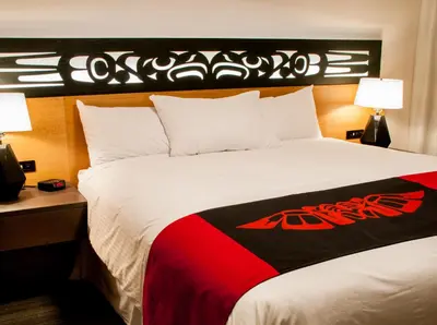 a hotel room with a large bed with a black and red blanket at Kwa'lilas Hotel in Port Hardy