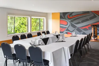 a conference room with tables and chairs and a mural at Kwa'lilas Hotel in Port Hardy