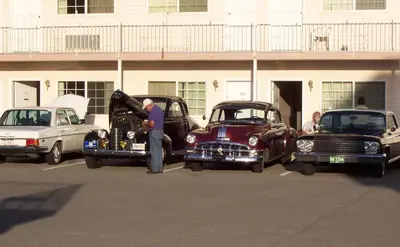 a man standing between two old cars in a parking lot at Model A Inn in Cranbrook