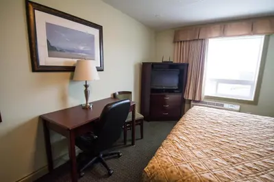 a hotel room with a desk and a bed and a television at Nova Inn Acheson in Spruce Grove