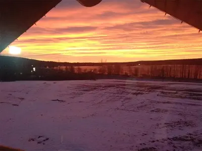 a sunset over a snow covered field with the sun setting at Cariboo Log Guest House in Lac La Hache