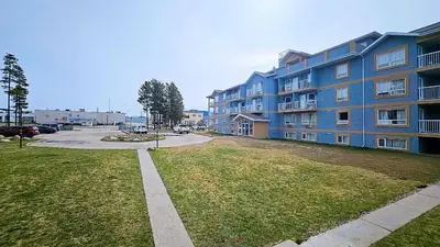a large blue apartment building with a grass yard at Misty Mountain Inn & Suites in Grande Cache