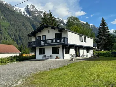 a large white house with mountains in the background at Bear Valley Guesthouse in Stewart