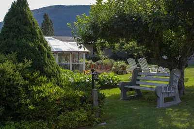 a park bench in a yard with a greenhouse at Genelle House B&B Guest House in Genelle