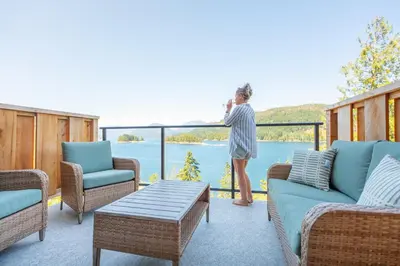 a woman standing on a balcony looking out at the water at West Coast Wilderness Lodge in Egmont