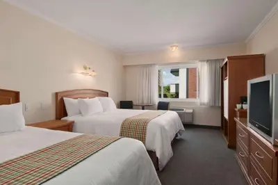 a hotel room with two beds and a flat screen tv at Travelodge by Wyndham Kamloops in Kamloops