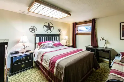a bedroom with a bed and a desk and a window at Rustlers Lodge in Sundre