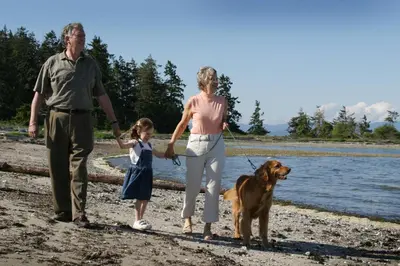 a man and a woman and a girl walking a dog on the beach at Oceanside Village Resort in Parksville