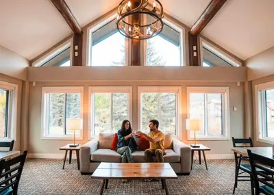 a man and woman sitting on a couch in a living room with windows at Basecamp Lodge Canmore in Canmore