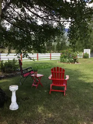 two red chairs and a table in a yard at Rose Cottage Bed & Breakfast in Valemount