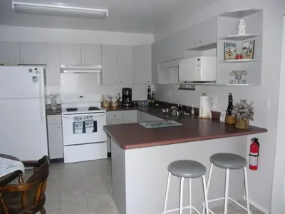 a kitchen with white appliances and two bar stools at Hammond Bay Oceanside Guesthouse in Nanaimo