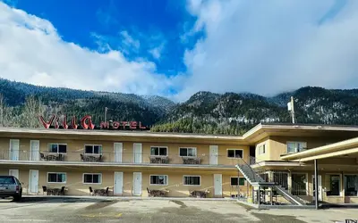 a hotel with a parking lot in front of a mountain at Villa Motel in Nelson