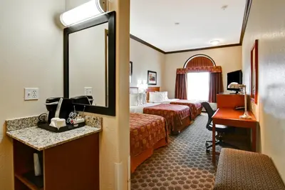 a hotel room with two beds and a desk and a mirror at Canalta Rocky Mountain House in Rocky Mountain House