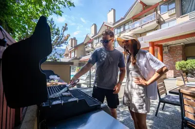a man and a woman standing next to a grill at Whistler Village Inn & Suites in Whistler