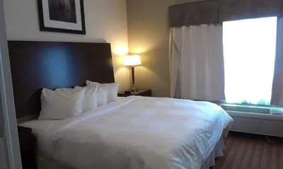a hotel room with a white bed and a window at Sigma Inn & Suites Hudson's Hope in Hudson Hope