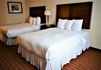 two beds in a hotel room with white sheets at Sigma Inn & Suites Hudson's Hope in Hudson Hope