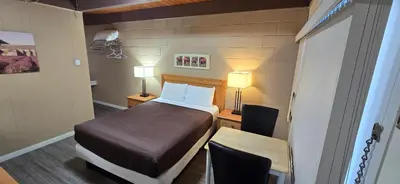 a bedroom with a bed and a desk with two lamps at Flamingo Motel in Penticton